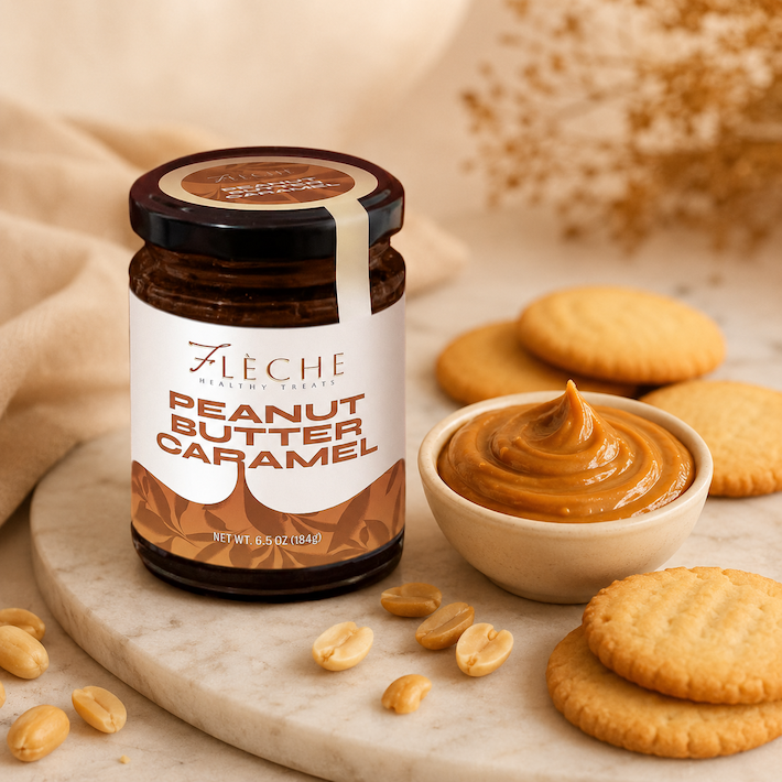 Jar of Fleche Peanut Butter Caramel with a bowl of peanut butter, cookies, and peanuts on a marble surface.