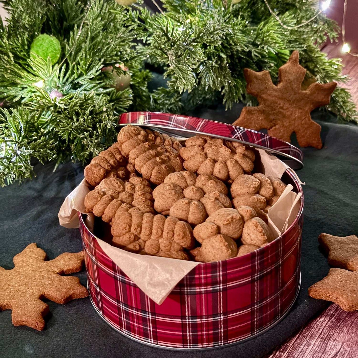 Crispy gluten-free spiced cookies in red plaid tin with dried orange slices and cinnamon sticks by Flèche Healthy Treats