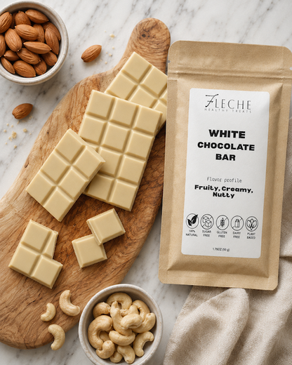 White chocolate bars on a wooden board with a package labeled 'Fleche' and bowls of nuts on a marble surface.